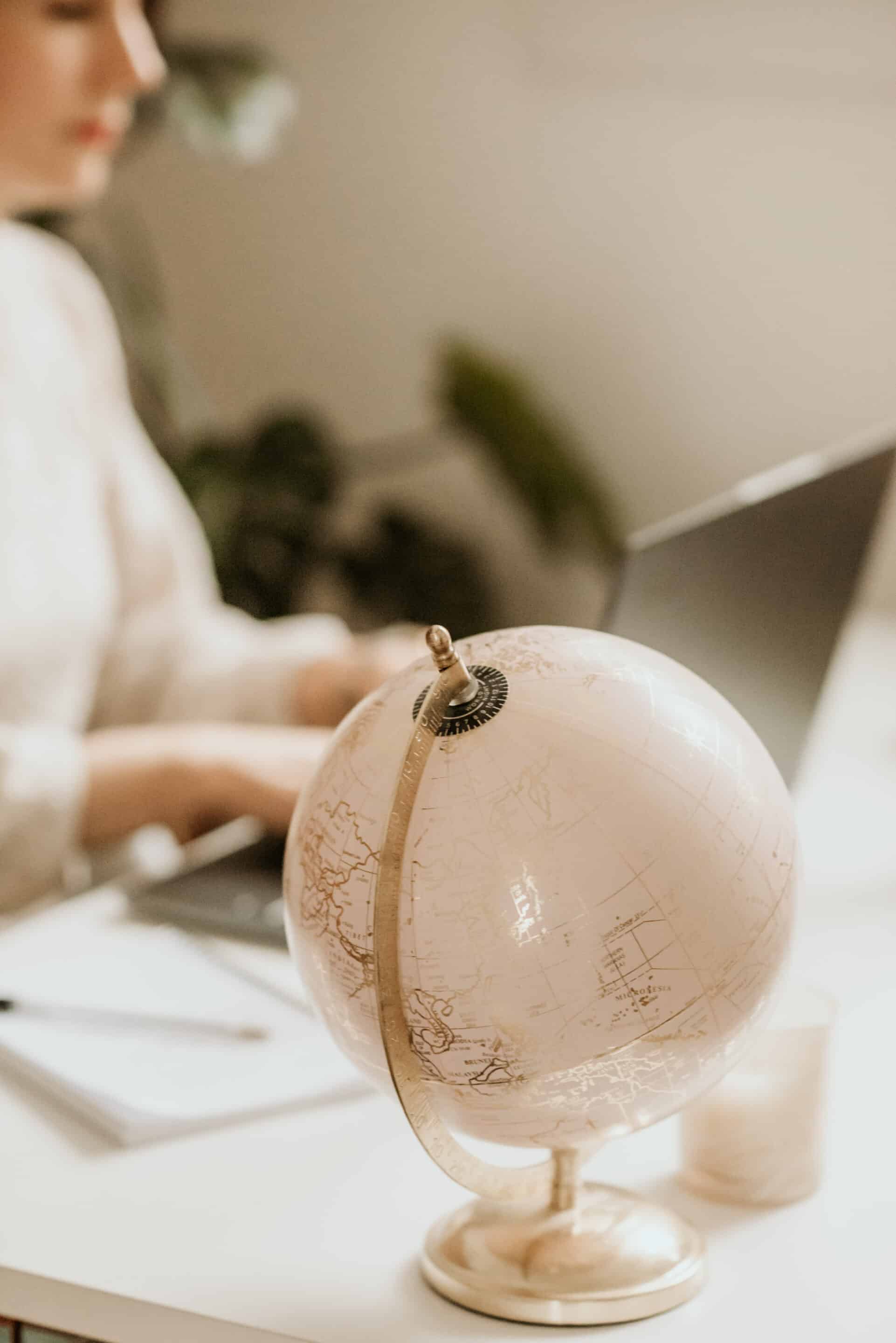 Marie-Léa en train de travailler sur le voyage de sa cliente sur son ordinateur, avec un globe beige en premier plan